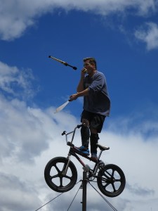Street entertainer juggling flame stick, sword and apple whilst balancing on a BMX on top of a pole!